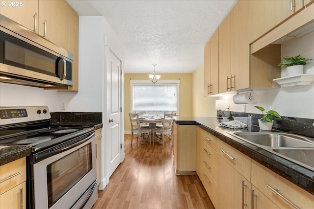 kitchen with light wood finished floors, light brown cabinetry, appliances with stainless steel finishes, a textured ceiling, and a sink