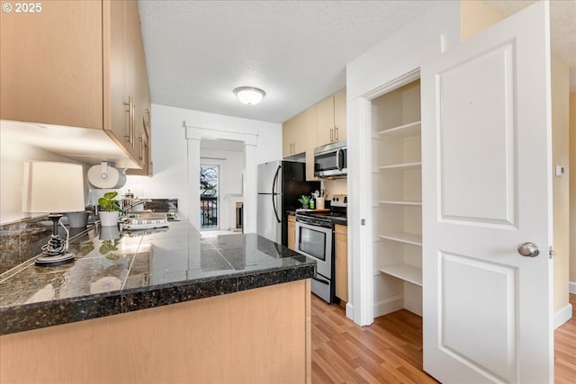 kitchen featuring a sink, tile counters, appliances with stainless steel finishes, a textured ceiling, and light wood-type flooring