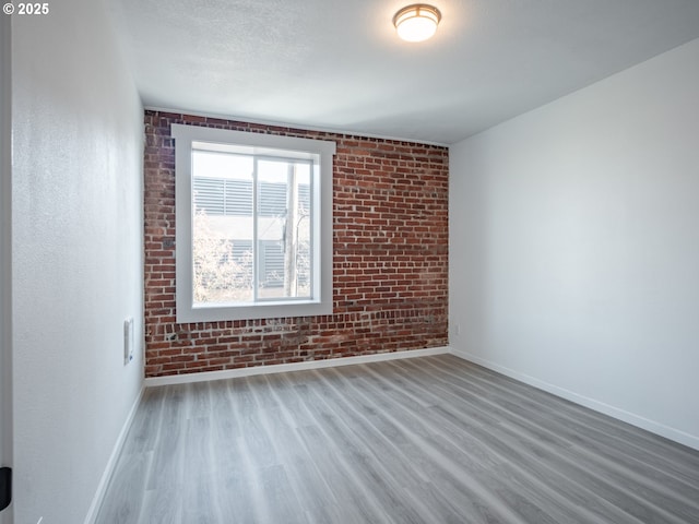 unfurnished room featuring baseboards, wood finished floors, and brick wall
