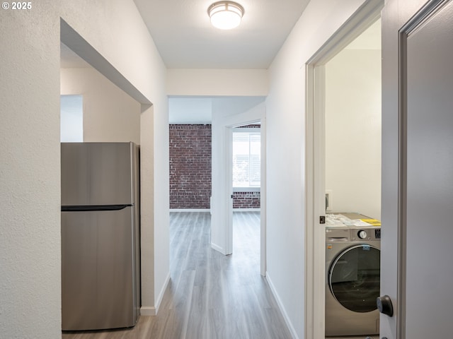 hallway with baseboards, washer / dryer, wood finished floors, and brick wall