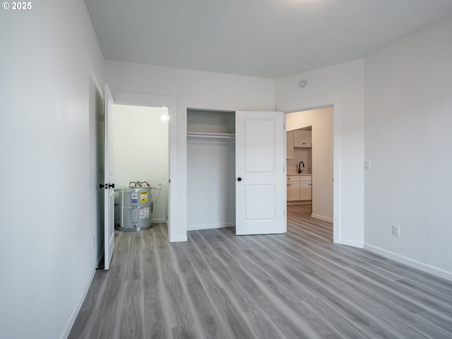 unfurnished bedroom with a sink, baseboards, electric water heater, wood finished floors, and a closet