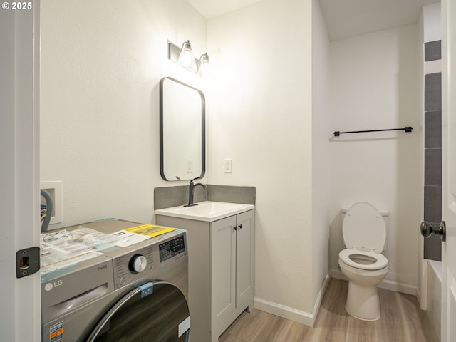 bathroom featuring vanity, wood finished floors, toilet, baseboards, and washer / clothes dryer