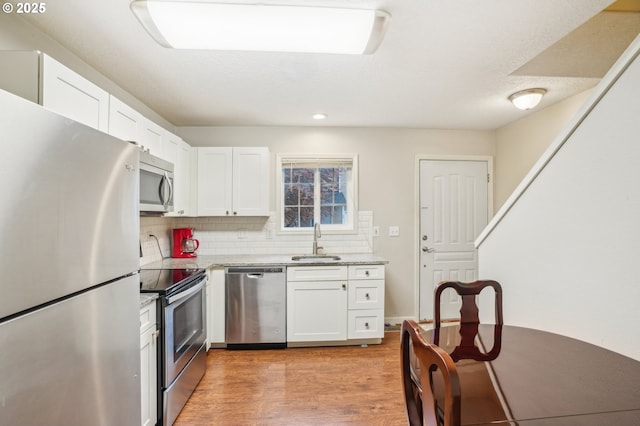 kitchen with stainless steel appliances, a sink, white cabinetry, decorative backsplash, and recessed lighting