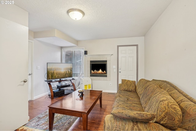 living room featuring wood finished floors, a tiled fireplace, a textured ceiling, and baseboards