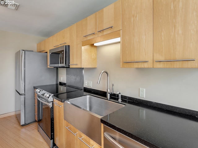 12600 SW Crescent St Unit 219, Beaverton, OR 97005 - kitchen with dark stone counters, light brown cabinets, a sink, light wood finished floors, and appliances with stainless steel finishes