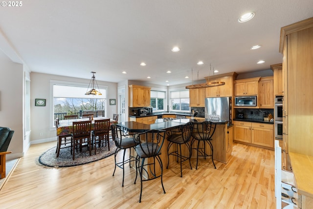 kitchen featuring a kitchen bar, light wood-type flooring, stainless steel appliances, a kitchen island, and hanging light fixtures