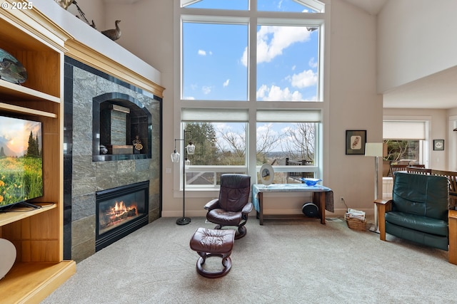 living area featuring a tile fireplace, carpet floors, a healthy amount of sunlight, and a high ceiling