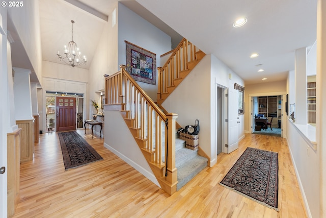 foyer with a towering ceiling, a chandelier, and light wood-type flooring