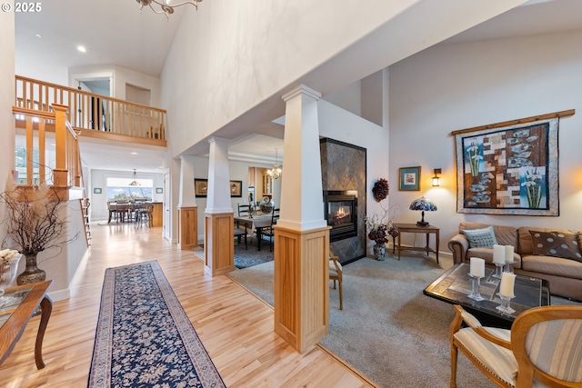 living room featuring a tile fireplace, an inviting chandelier, light wood-type flooring, ornate columns, and a towering ceiling