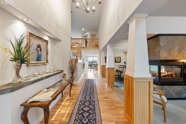 hall with decorative columns, light hardwood / wood-style flooring, a towering ceiling, and a chandelier