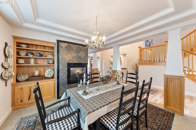 carpeted dining room featuring built in shelves, ornamental molding, a tray ceiling, a notable chandelier, and a tiled fireplace