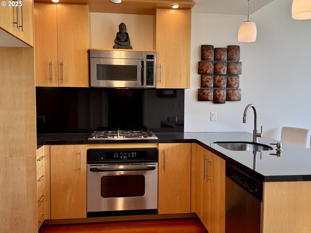 kitchen with a peninsula, dark countertops, appliances with stainless steel finishes, a sink, and hanging light fixtures