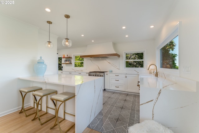 kitchen with kitchen peninsula, premium range hood, white cabinets, decorative light fixtures, and backsplash