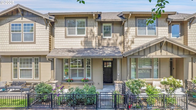 townhome / multi-family property with a porch, a fenced front yard, a gate, and roof with shingles