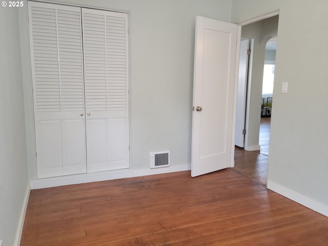 unfurnished bedroom featuring arched walkways, baseboards, visible vents, and a closet