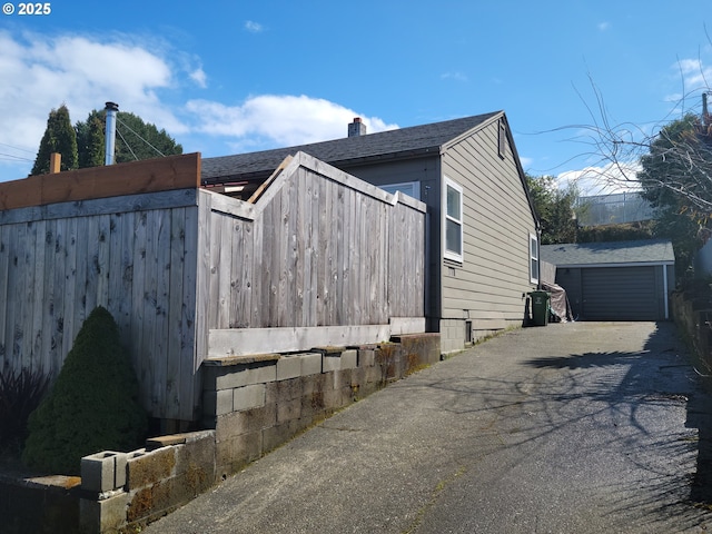 view of side of home with a detached garage, fence, an outdoor structure, and roof with shingles