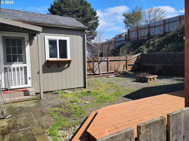 view of yard with an outbuilding, a fire pit, a fenced backyard, and a wooden deck