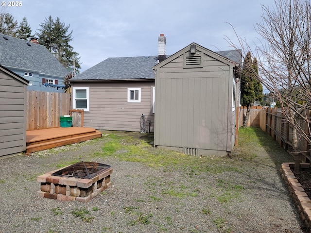 rear view of property featuring roof with shingles, a deck, a fenced backyard, a shed, and a fire pit