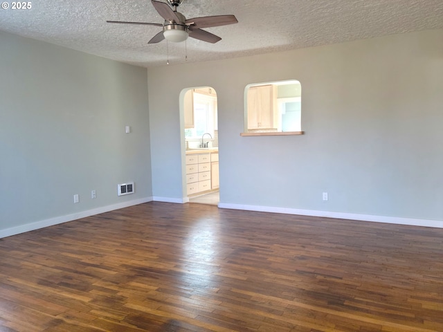 unfurnished room featuring a ceiling fan, a textured ceiling, visible vents, arched walkways, and dark wood-style floors