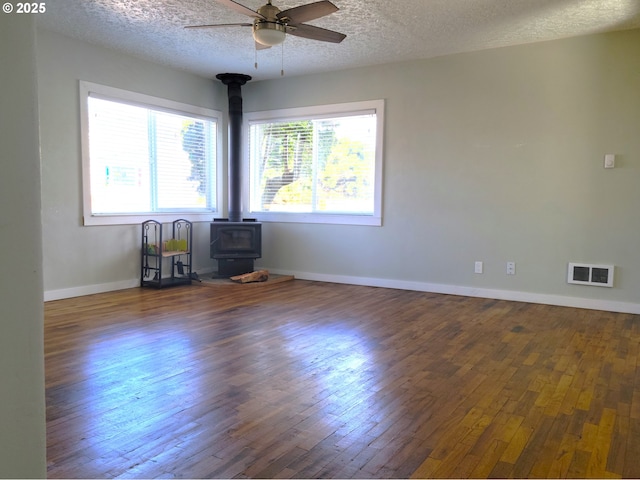 empty room featuring visible vents, a wood stove, a ceiling fan, and hardwood / wood-style flooring