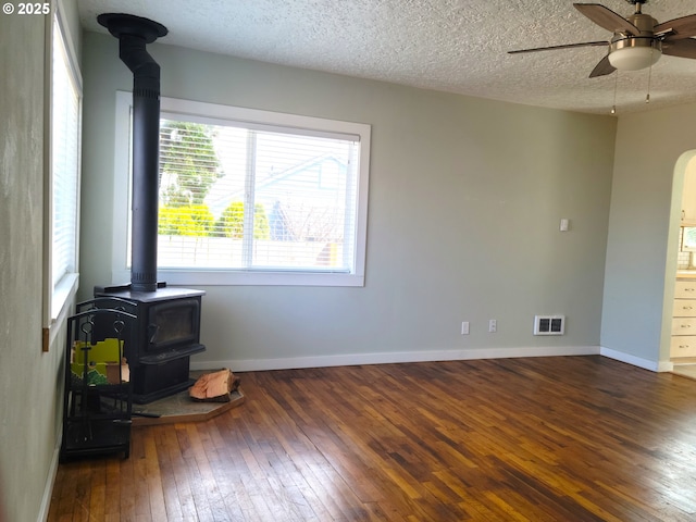 spare room featuring ceiling fan, a textured ceiling, arched walkways, a wood stove, and hardwood / wood-style flooring