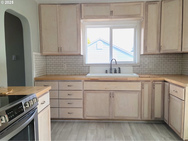 kitchen featuring light brown cabinetry, electric range, a sink, light countertops, and backsplash