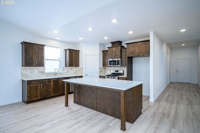 kitchen with stainless steel appliances, tasteful backsplash, a center island, light wood-type flooring, and sink