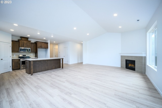 kitchen featuring light hardwood / wood-style floors, stainless steel appliances, lofted ceiling, a fireplace, and a kitchen island