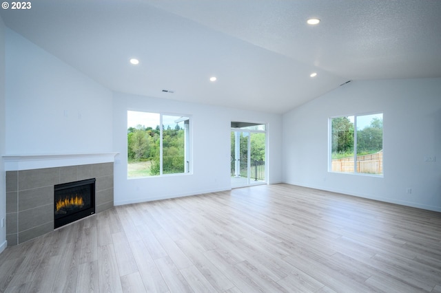 unfurnished living room featuring light hardwood / wood-style floors, a tile fireplace, a healthy amount of sunlight, and vaulted ceiling