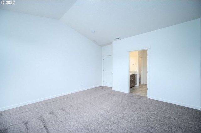 unfurnished bedroom with vaulted ceiling, carpet flooring, and ensuite bath