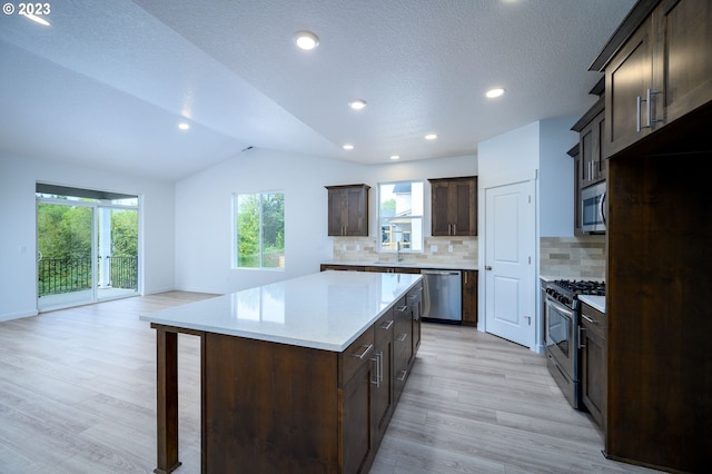 kitchen with lofted ceiling, backsplash, appliances with stainless steel finishes, and a center island