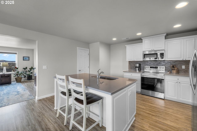 kitchen featuring a kitchen island with sink, sink, light hardwood / wood-style flooring, appliances with stainless steel finishes, and white cabinetry