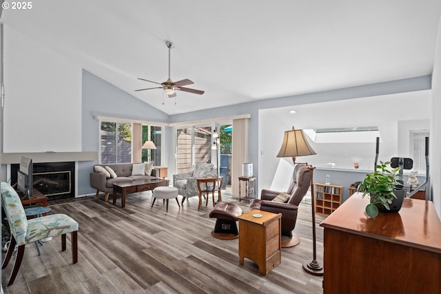 living room with wood finished floors, vaulted ceiling, a ceiling fan, and a glass covered fireplace