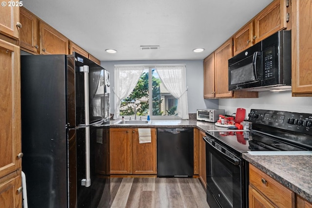 kitchen featuring black appliances, a sink, light wood-style flooring, brown cabinets, and recessed lighting