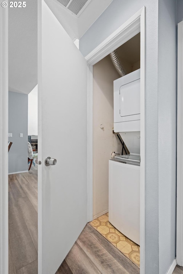 clothes washing area featuring stacked washer / drying machine and wood finished floors