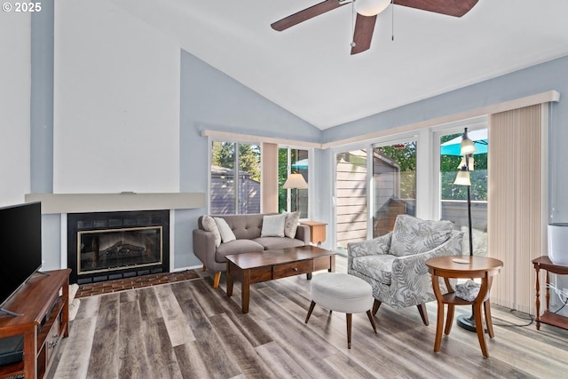living room with wood finished floors, ceiling fan, a glass covered fireplace, and high vaulted ceiling