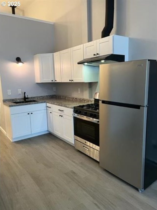 1127 6th Ave, Albany, OR 97321 - kitchen featuring stainless steel appliances, under cabinet range hood, white cabinets, light wood-style flooring, and a towering ceiling