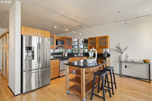 kitchen with track lighting, stainless steel appliances, a kitchen breakfast bar, and light wood-type flooring