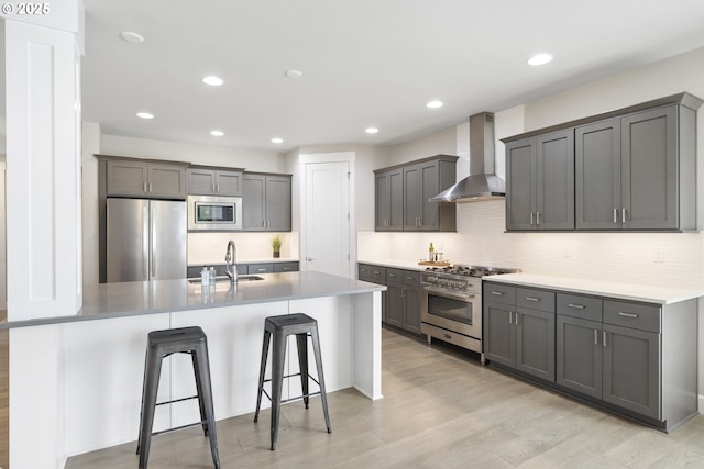 21338 SW Simon Ter, Sherwood, OR 97140 - kitchen featuring wall chimney range hood, appliances with stainless steel finishes, a kitchen bar, light wood-style flooring, and backsplash
