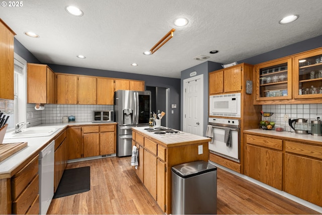 7820 SE 114th Ave, Portland, OR 97266 - kitchen featuring white appliances, light wood-type flooring, a center island, a sink, and a textured ceiling