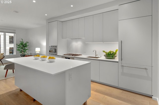 kitchen with wall oven, light countertops, light wood-type flooring, stainless steel gas stovetop, and a sink