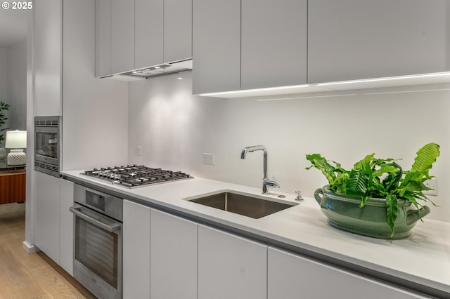 kitchen featuring a sink, stainless steel appliances, under cabinet range hood, white cabinetry, and modern cabinets