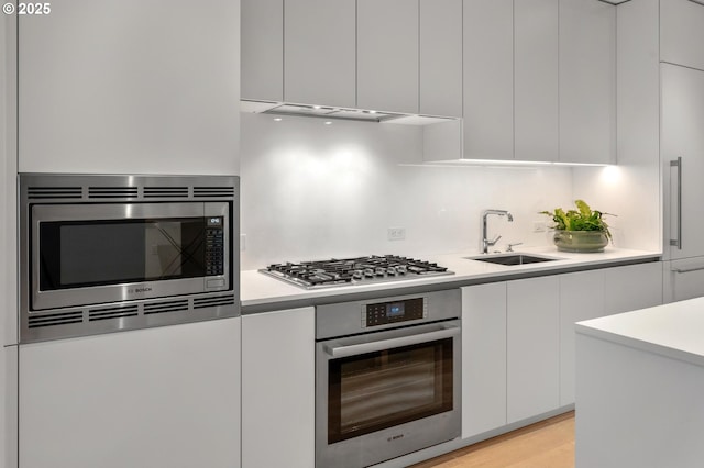 kitchen with modern cabinets, a sink, white cabinetry, appliances with stainless steel finishes, and light countertops