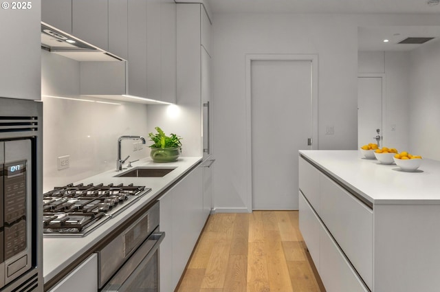 kitchen featuring oven, light wood-type flooring, modern cabinets, a sink, and stainless steel gas cooktop