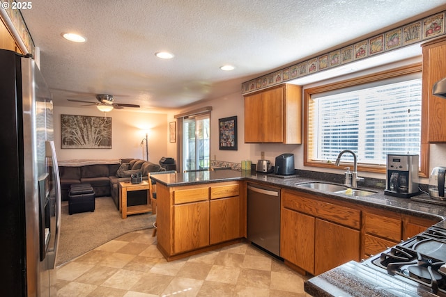 kitchen with open floor plan, brown cabinets, a peninsula, stainless steel appliances, and a sink