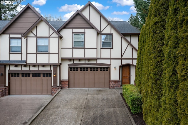 tudor-style house with an attached garage, concrete driveway, and brick siding