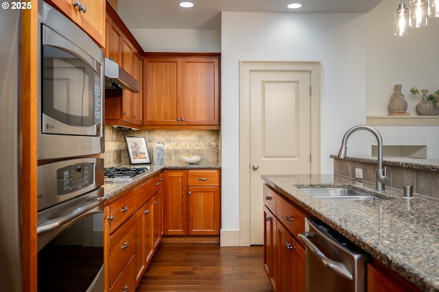 kitchen with dark wood-style flooring, under cabinet range hood, tasteful backsplash, a sink, and appliances with stainless steel finishes