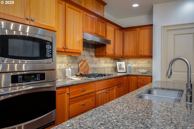 kitchen featuring decorative backsplash, brown cabinetry, appliances with stainless steel finishes, a sink, and under cabinet range hood