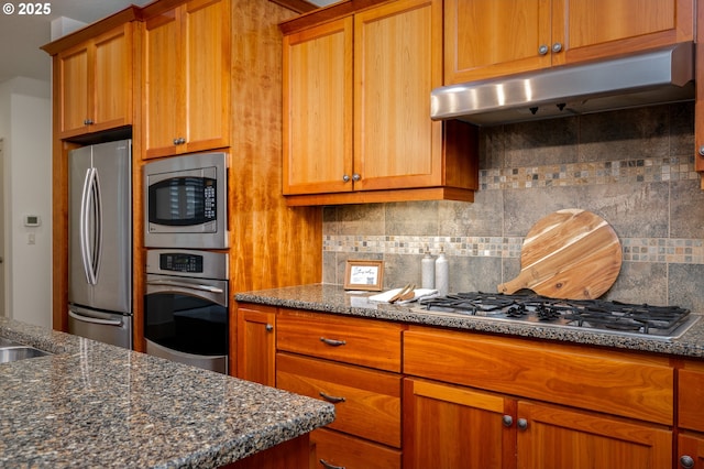 kitchen with under cabinet range hood, stainless steel appliances, brown cabinets, and backsplash