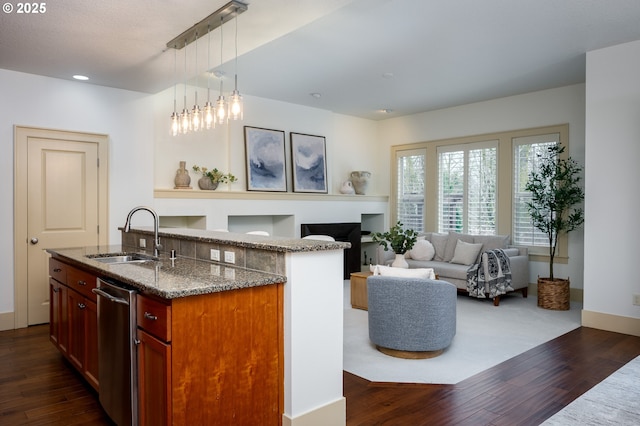 kitchen with hanging light fixtures, a sink, dark stone counters, stainless steel dishwasher, and dark wood-style floors